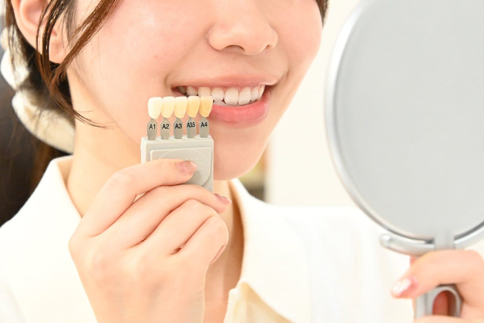 シェードガイドと鏡で歯の色を確認する様子